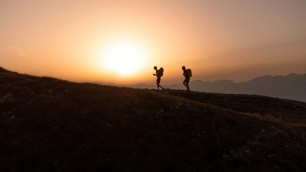 Two men walking along a ridge in the Swiss mountains while the sun is setting.